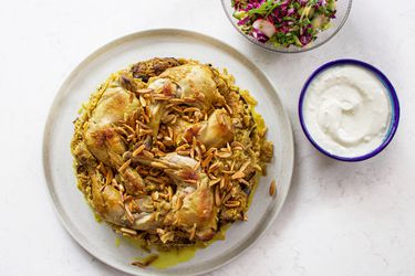 Maqlubeh plated on a white dish with a bowl of sauce and a small salad next to it