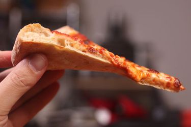 一只手举着一块自制的纽约奶酪披萨。