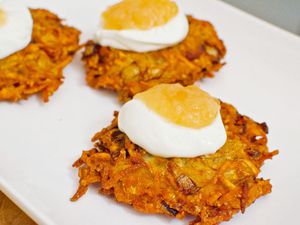Latkes on a platter topped with sour cream and applesauce.