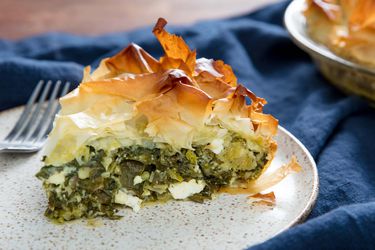 A wedge of spanakopita on a speckled white plate with a fork.