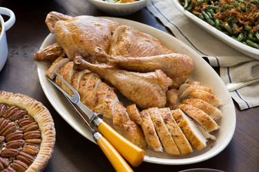 A platter of carved turkey with a carving knife and fork, surrounded by pecan pie, green bean casserole, and salad.