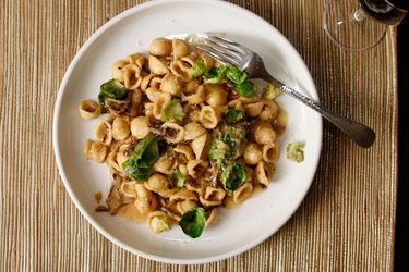 A plate of orecchiette with mushrooms and Brussels sprouts with a glass of wine in the background