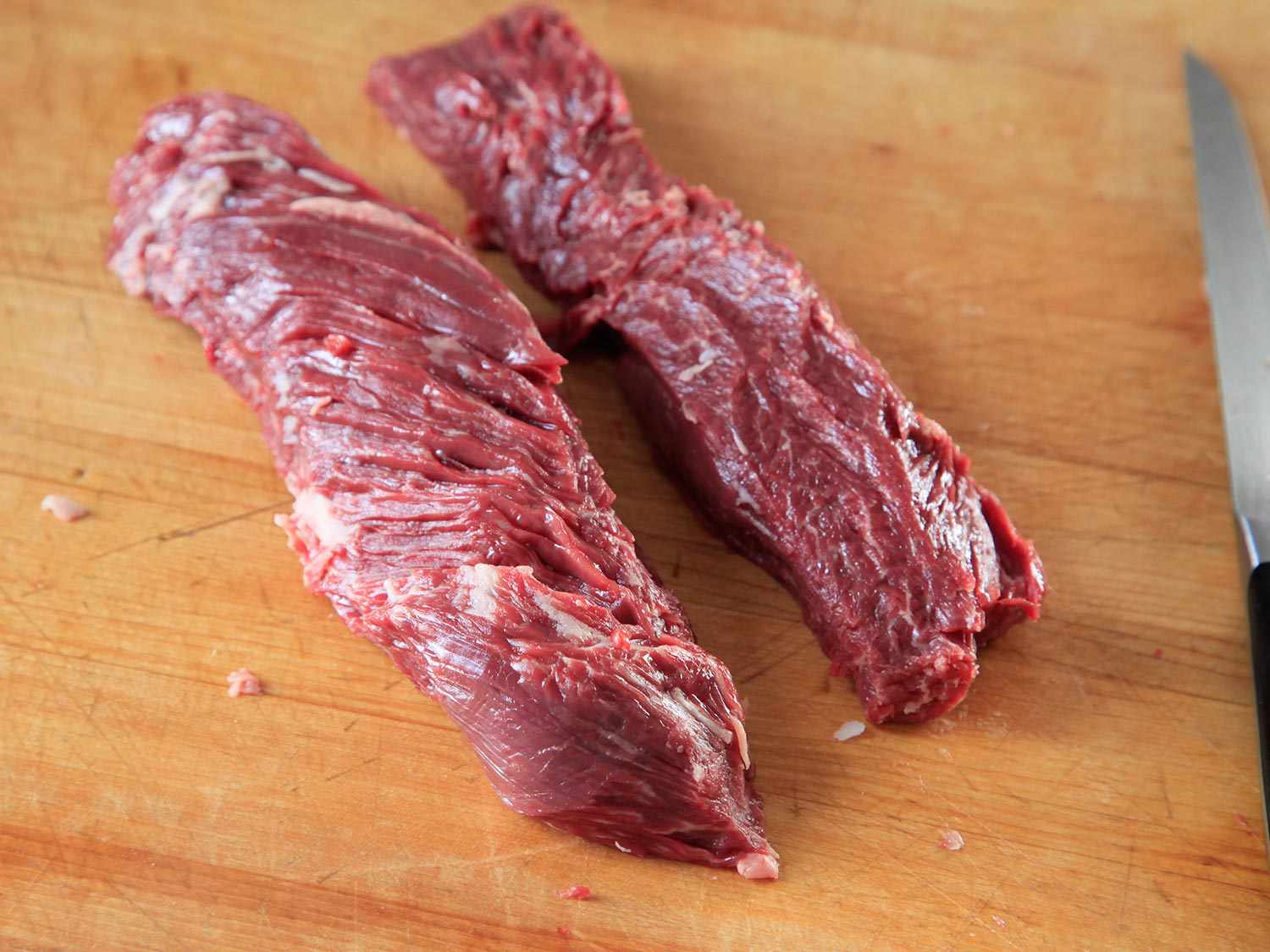 Two pieces of raw hanger steak on a wooden surface