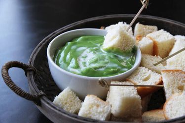 A bowl of Thai coconut dip set on a platter with cubes of bread and small skewers.