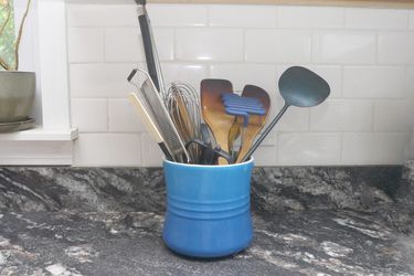 a blue utensil crock full of wooden spoons and spatulas on a dark marble counter
