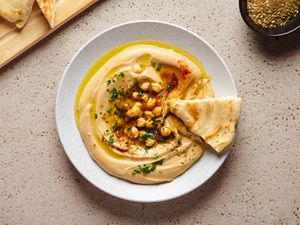 The best smooth hummus in a white round dish, with a piece of pita bread on the right hand side of the plate.