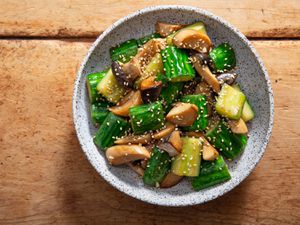 Overhead view of stir-fried cucumbers with trumpet mushrooms, garnished with sesame seeds and served in a speckled earthenware bowl.