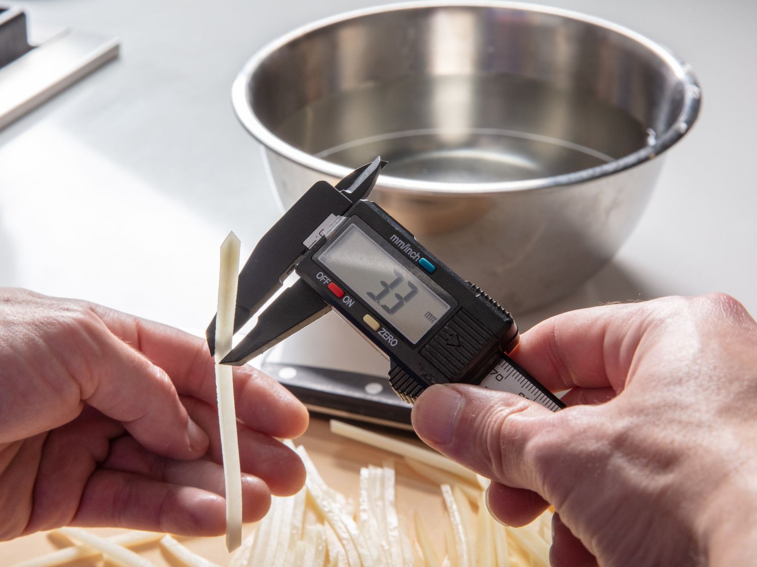 Hands holding pair of digital calipers, which are being used to measure thickness of a shoestring fry