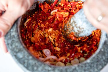 Using a mortar and pestle to grind chiles and shallots.