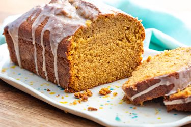 A loaf of pumpkin bread topped with glaze on a tray. A few slices are on the tray next to the loaf.