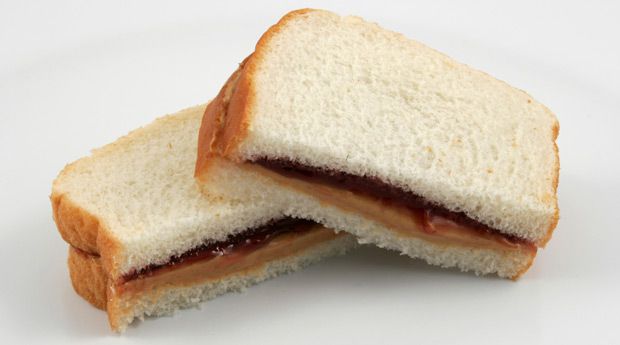 花生黄油和果冻三明治放在切片白面包上，切成两半，切好的一面对着镜头。