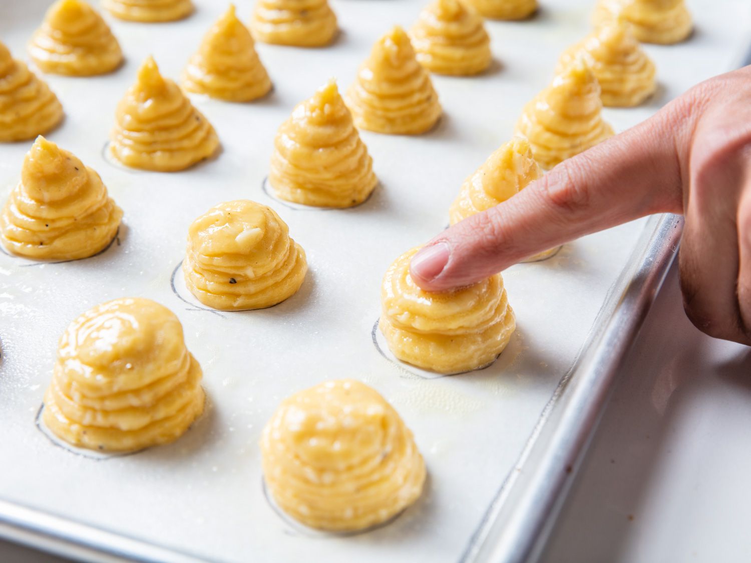 A moist finger press down on the piped mounds of choux paste.