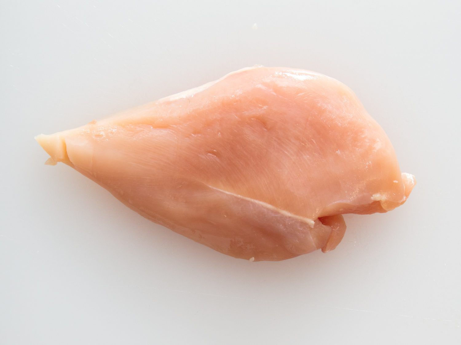 A boneless, skinless chicken breast on a plastic cutting board.