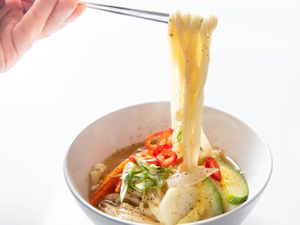 A bowl of Korean knife-cut noodle soup, showing chopsticks lifting noodles from the bowl below.
