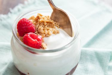 A glass jar with thick homemade yogurt, granola, and raspberries.