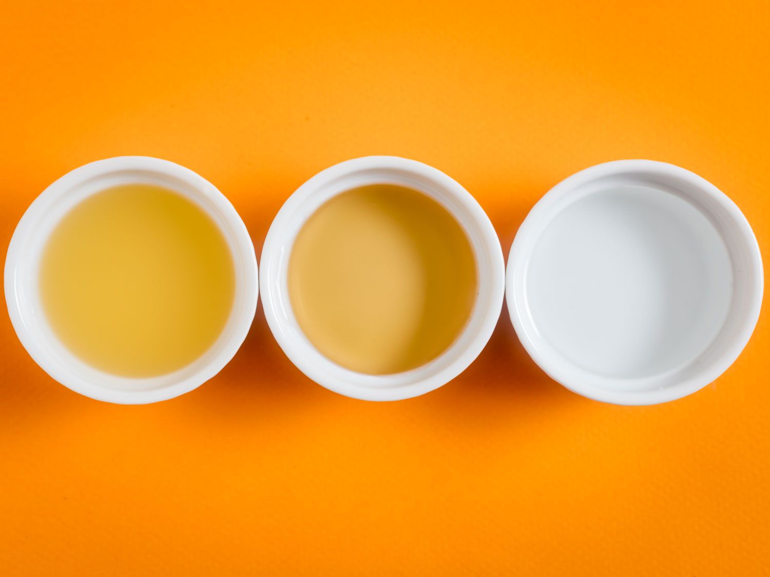 头顶上的三种不同醋的白色杯子，以橙色为背景