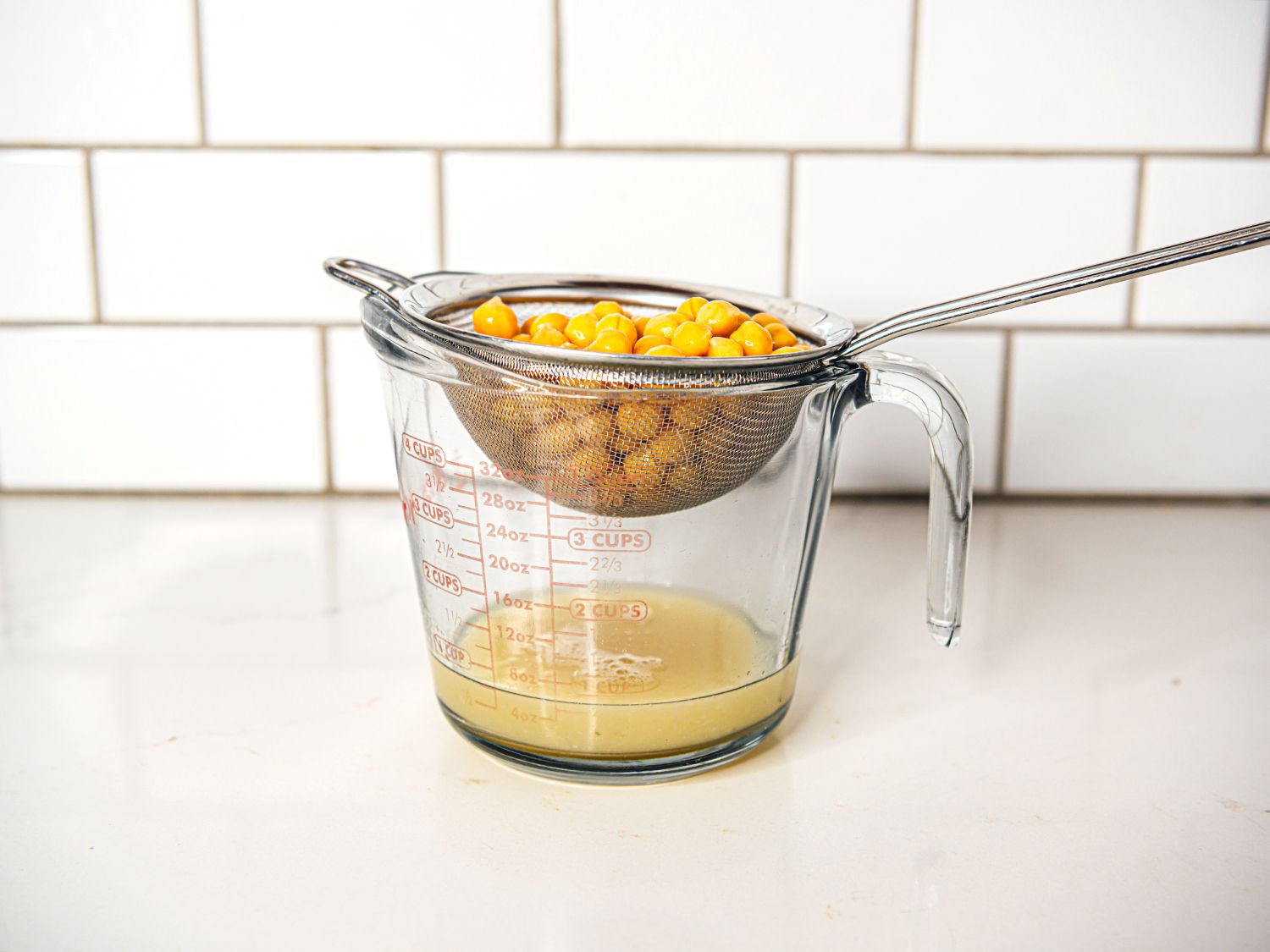 a can of chickpeas draining their liquid (aquafaba) into a glass measuring cup