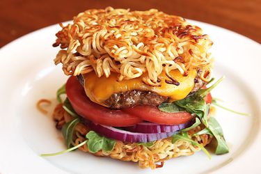 Cheeseburger with baby greens and sliced tomato and red onion, sandwiched between two pan-fried ramen 