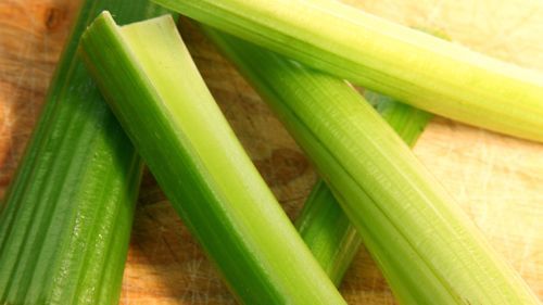 Close up photo of celery stalks on wooden surface.