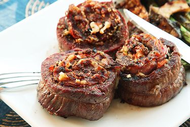 Stuffed and grilled flank steaks on white platter with asparagus and mushrooms