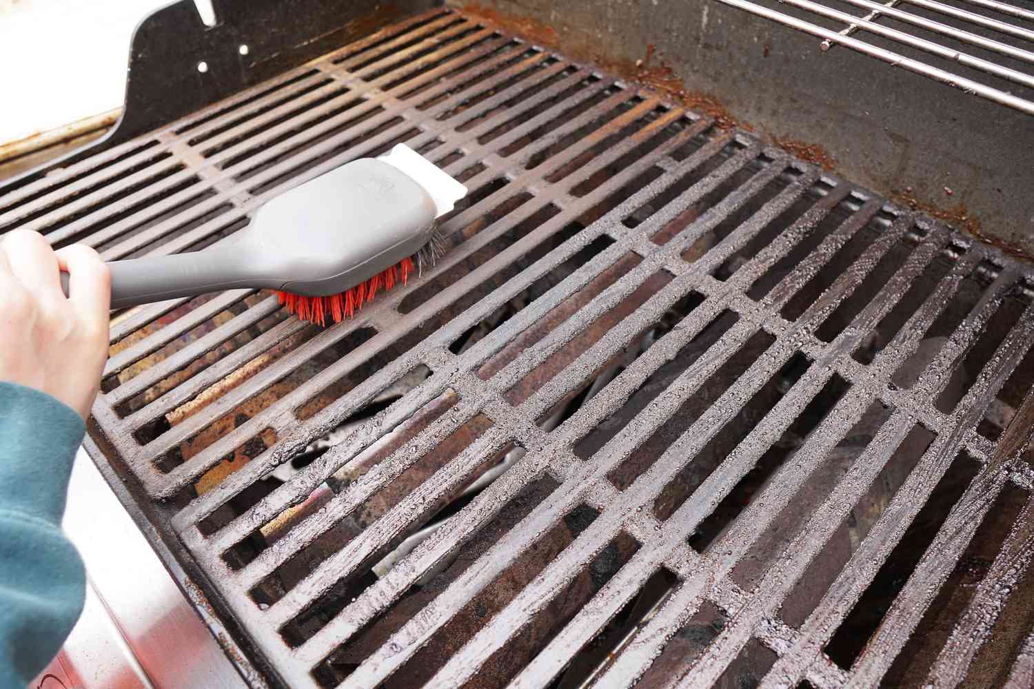 A closeup look at a grill brush scrubbing down a grill grate