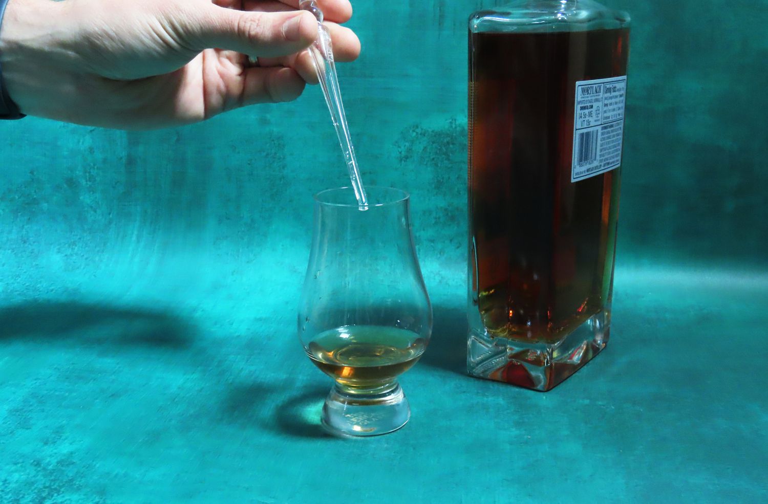 A person using a whisky pipette to dilute whisky in a glass