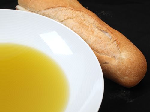 一碗橄榄油的特写，旁边是一大块不新鲜的法棍面包。