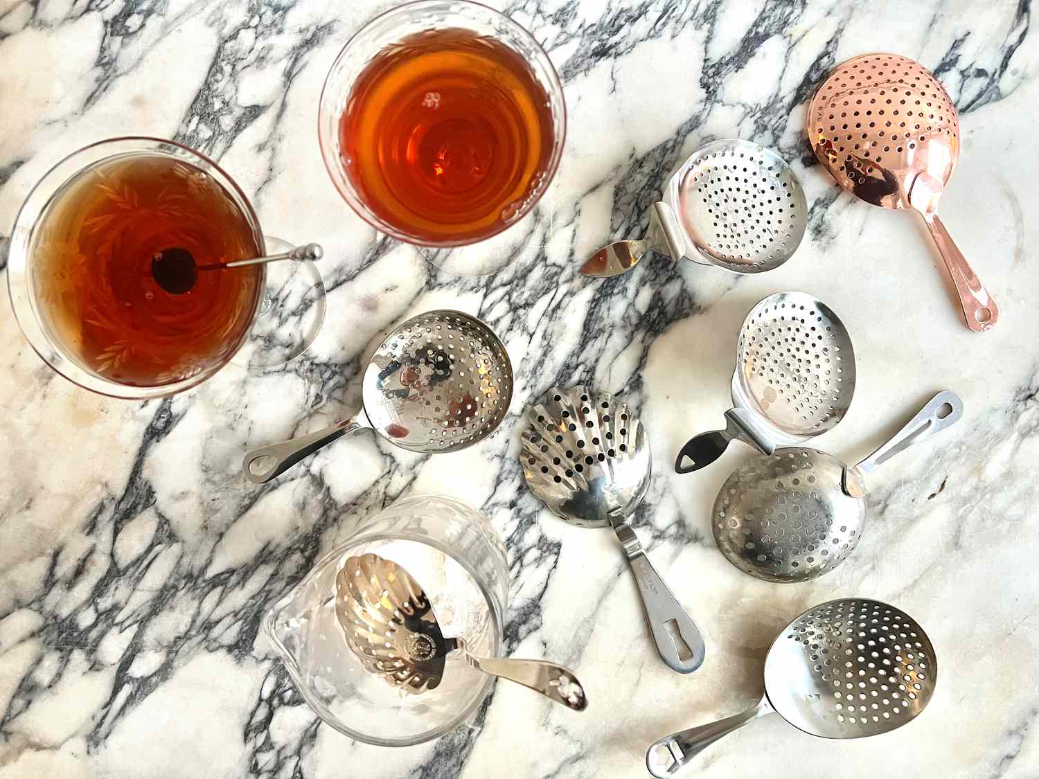 a variety of julep strainers with two cocktails on a marble countertop