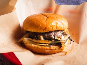 一个俄克拉荷马风格的洋葱汉堡，用熟食纸包装，装在红色的塑料熟食篮子里。