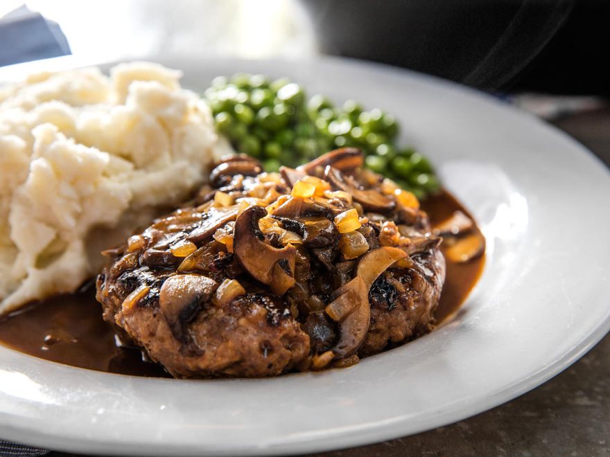 A Salisbury steak smothered in mushroom gravy with mashed potatoes and peas
