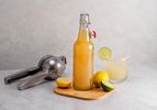 在木砧板上放一瓶酸果汁，柠檬，切片酸橙，柑橘榨汁机，一杯混合饮料。
