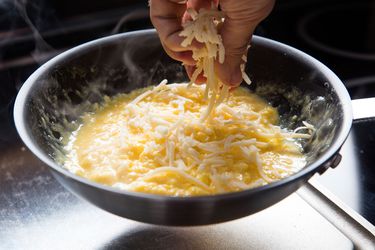 Sprinkling grated cheese into a pan of scrambling eggs