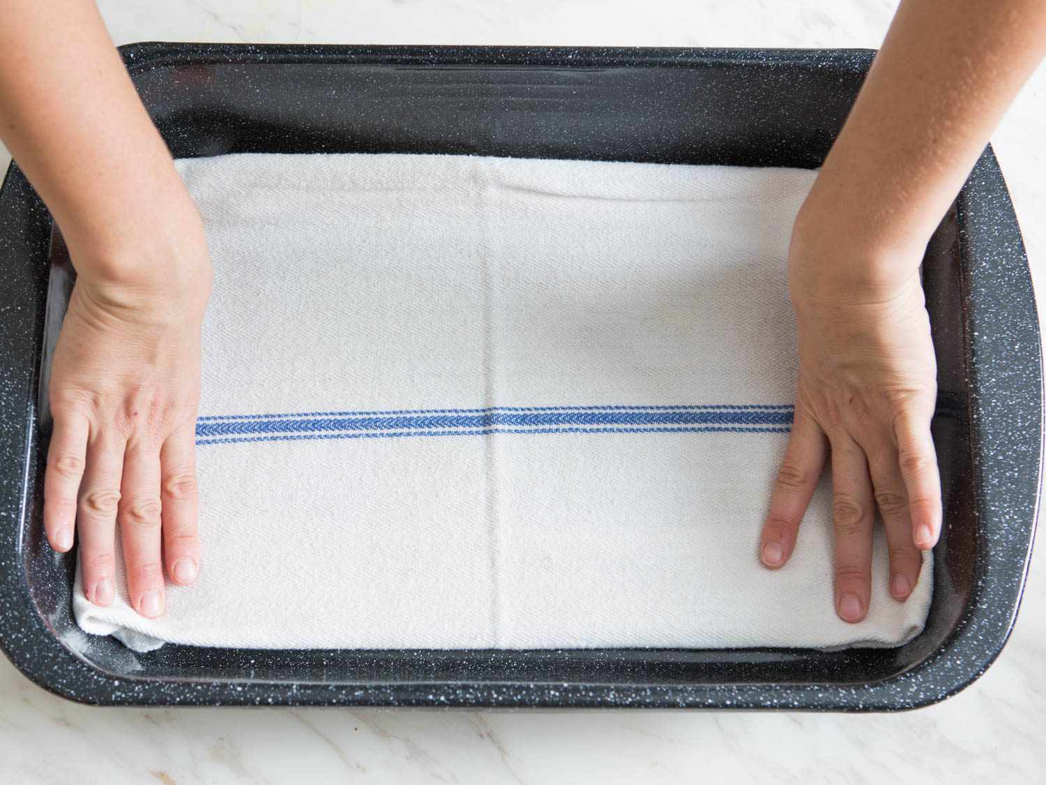 A blue and white cotton towel being placed into the bottom of a roasting pan