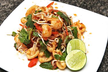 Isan-style spicy Thai fried pork rind salad, served on a square white plate with lime halves.