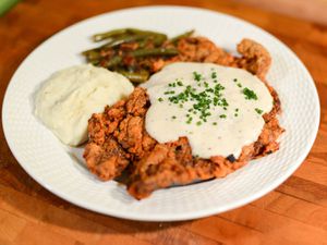 A plate of chicken-fried steak with gravy, potatoes, and vegetable.