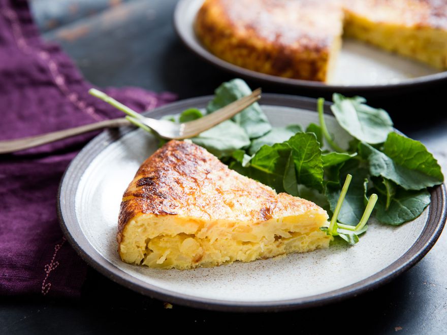 A slice of Spanish potato and onion tortilla on a small grey plate with salad on the side.