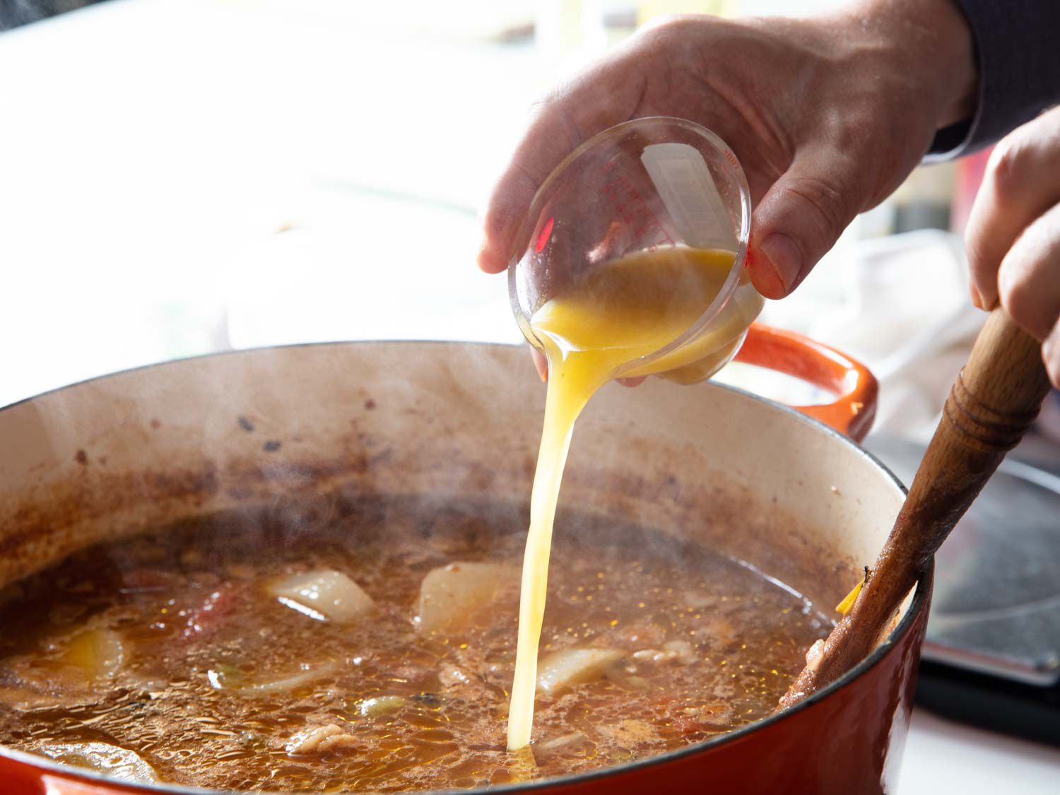 an oxo mini measuring cup being used to pour liquid into a pot of cooking stew