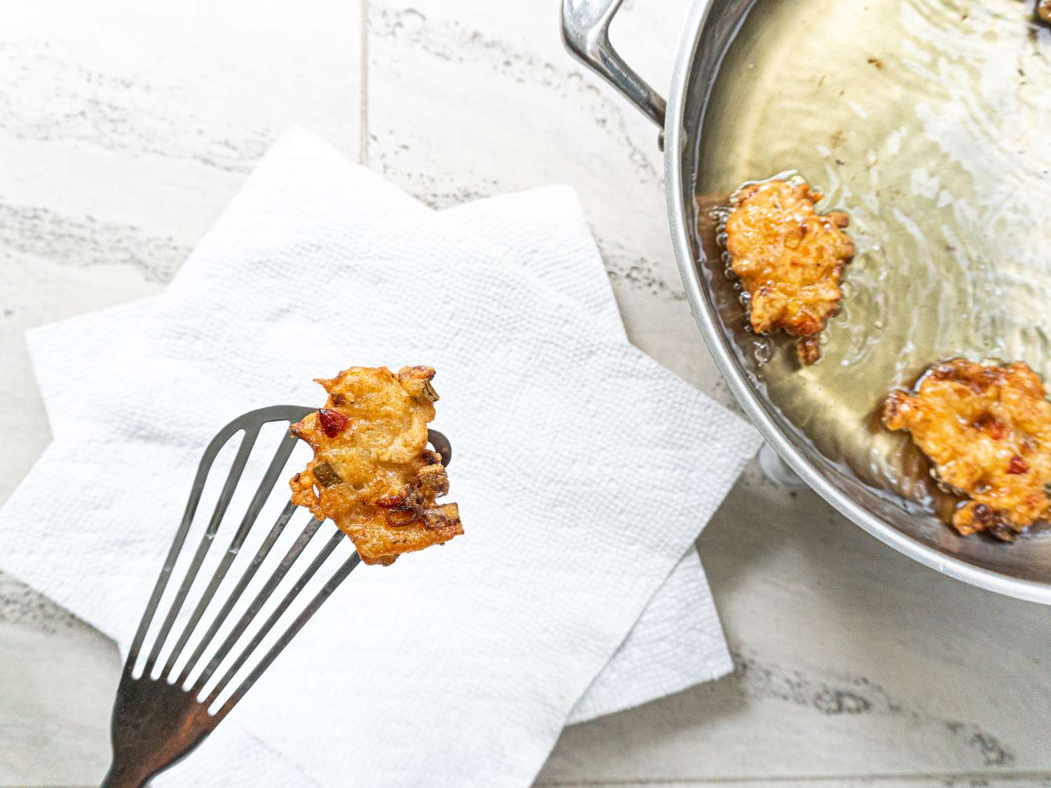 Slotted spatula removing fritters from a frying pan.