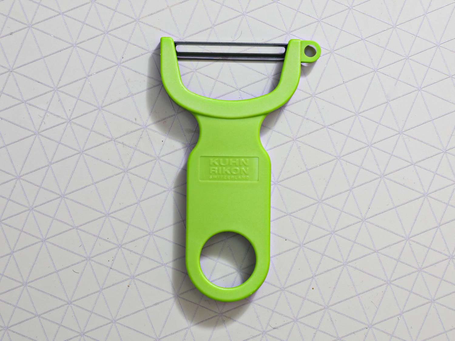 A green vegetable peeler on a grey surface