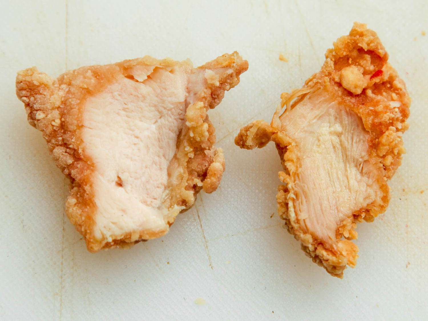Fried chicken breast (left) and fried chicken thigh (right) side-by-side on white cutting board.
