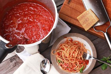 头顶上的一锅高压锅番茄酱，一碗拌着番茄酱的意大利面，大块的帕尔马干酪放在奶酪磨碎器上
