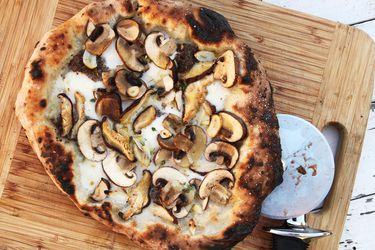 俯视图，一个蘑菇松露披萨放在砧板上，准备切片和服务。
