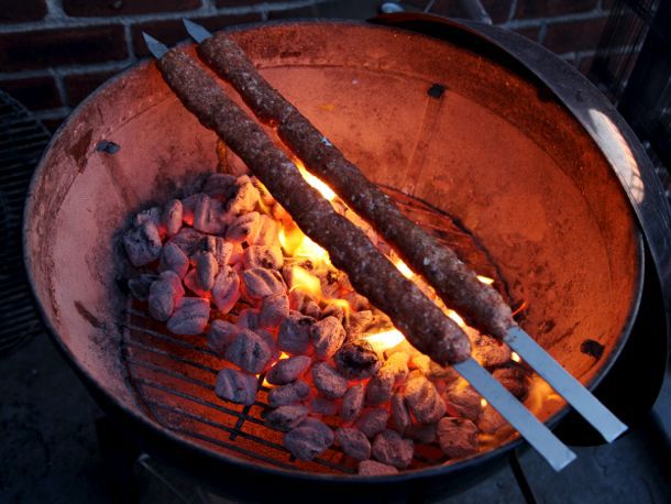 阿达纳烤肉串在木炭上烤。又宽又扁的金属烤串足够长，可以放在整个水壶上，就不需要烧烤格栅了。