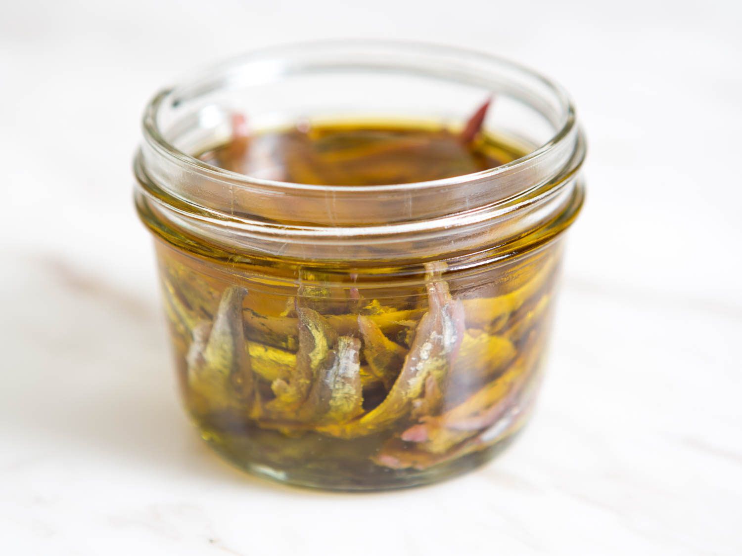 Small jar of anchovies in oil against white background.