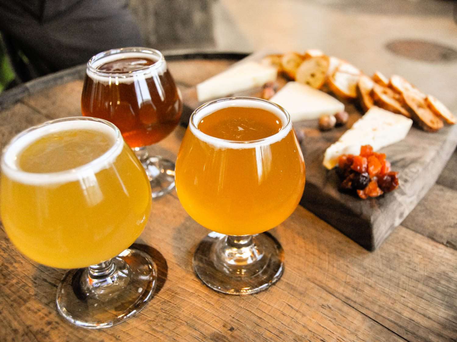 Three different beers in glasses next to a cheese board.