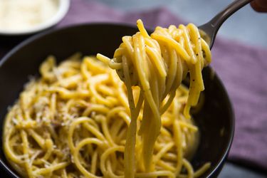 Close-up of spaghetti carbonara twirled on a fork above a serving bowl.