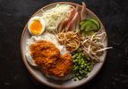 Overhead of a serving plate of noodles dressed with fish curry, with assorted vegetable garnishes and a soft-cooked egg on the side.