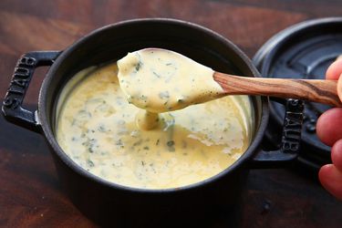 Béarnaise sauce being scooped out of a small cast iron pot with a wooden spoon