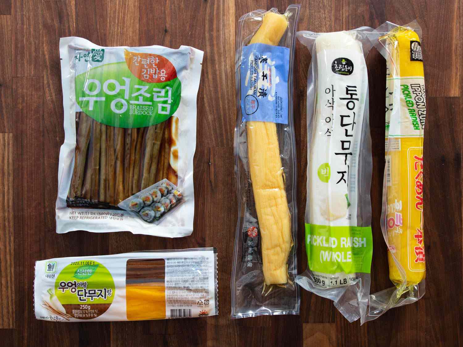 At right, pickled whole radish in three colors (beige, white, and yellow). At left on top, braised burdock in its own package. At left on the bottom, a combo pack of pickled daikon strips and braised burdock, ready for kimbap.