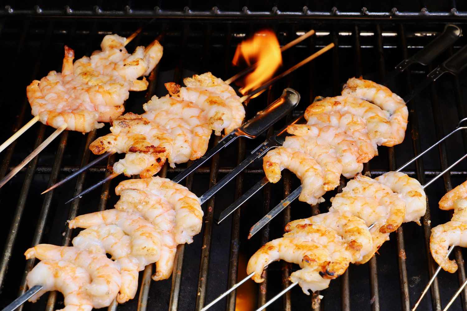 a mix of bamboo and stainless steel shrimp skewers cooking on a gas grill